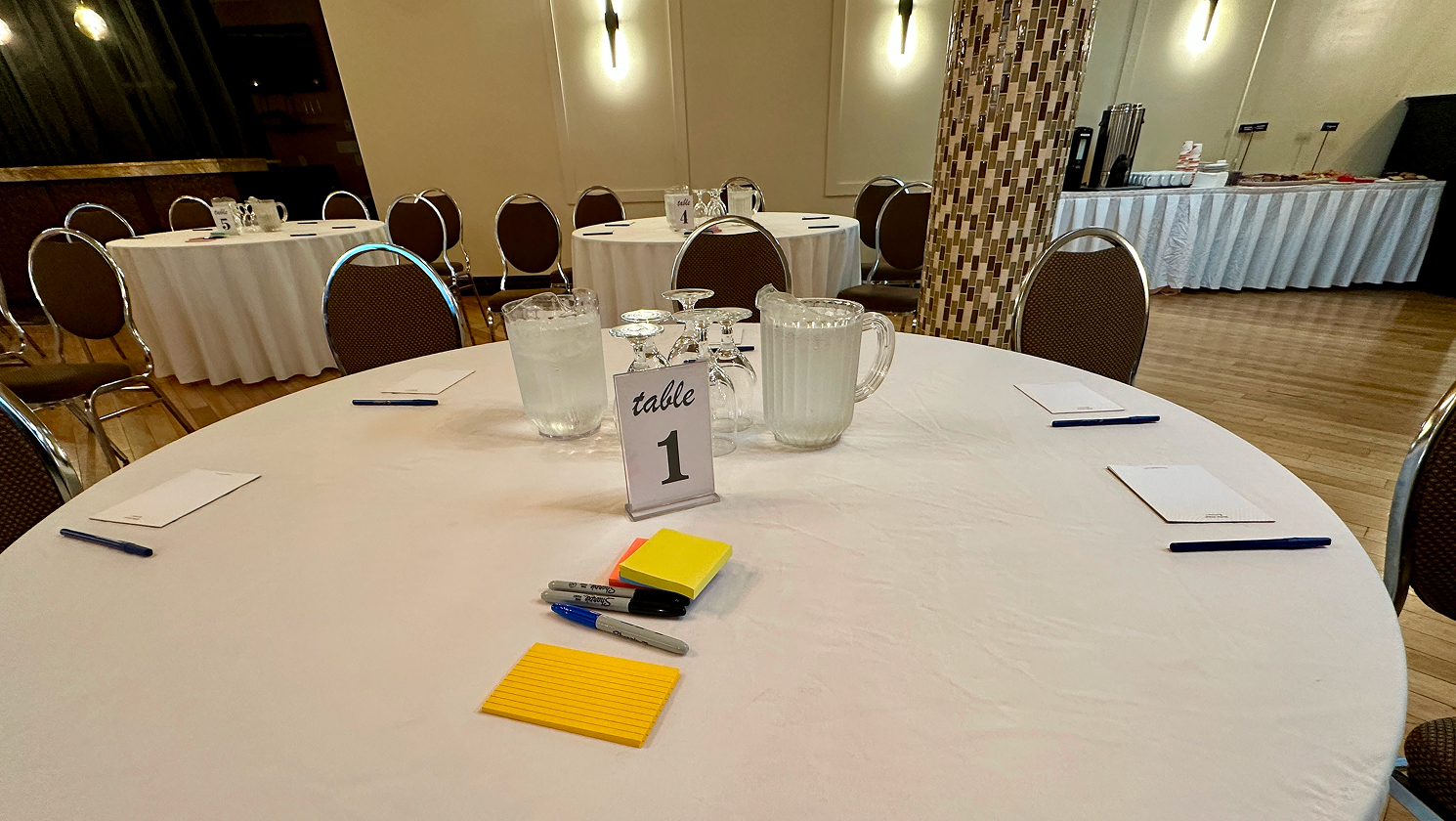 Before participants arrived, workshop tables were set with sticky notes, markers, and notepads at each seat.