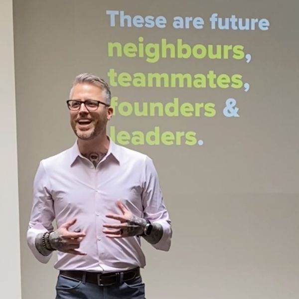 Jamie Gerrard presenting beside a projected slide reading These are future neighbours, teammates, founders and leaders.