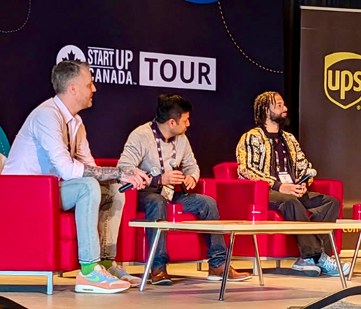 Three men are seated in red armchairs on stage at the Startup Canada Tour in Halifax.