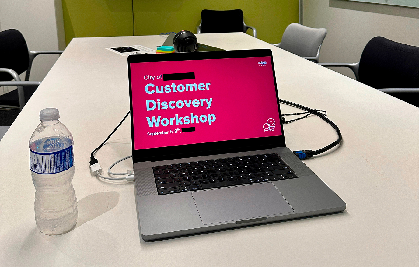 Laptop on a boardroom table showing the title of a slide for a municipal government customer discovery workshop, with the city's name redacted.