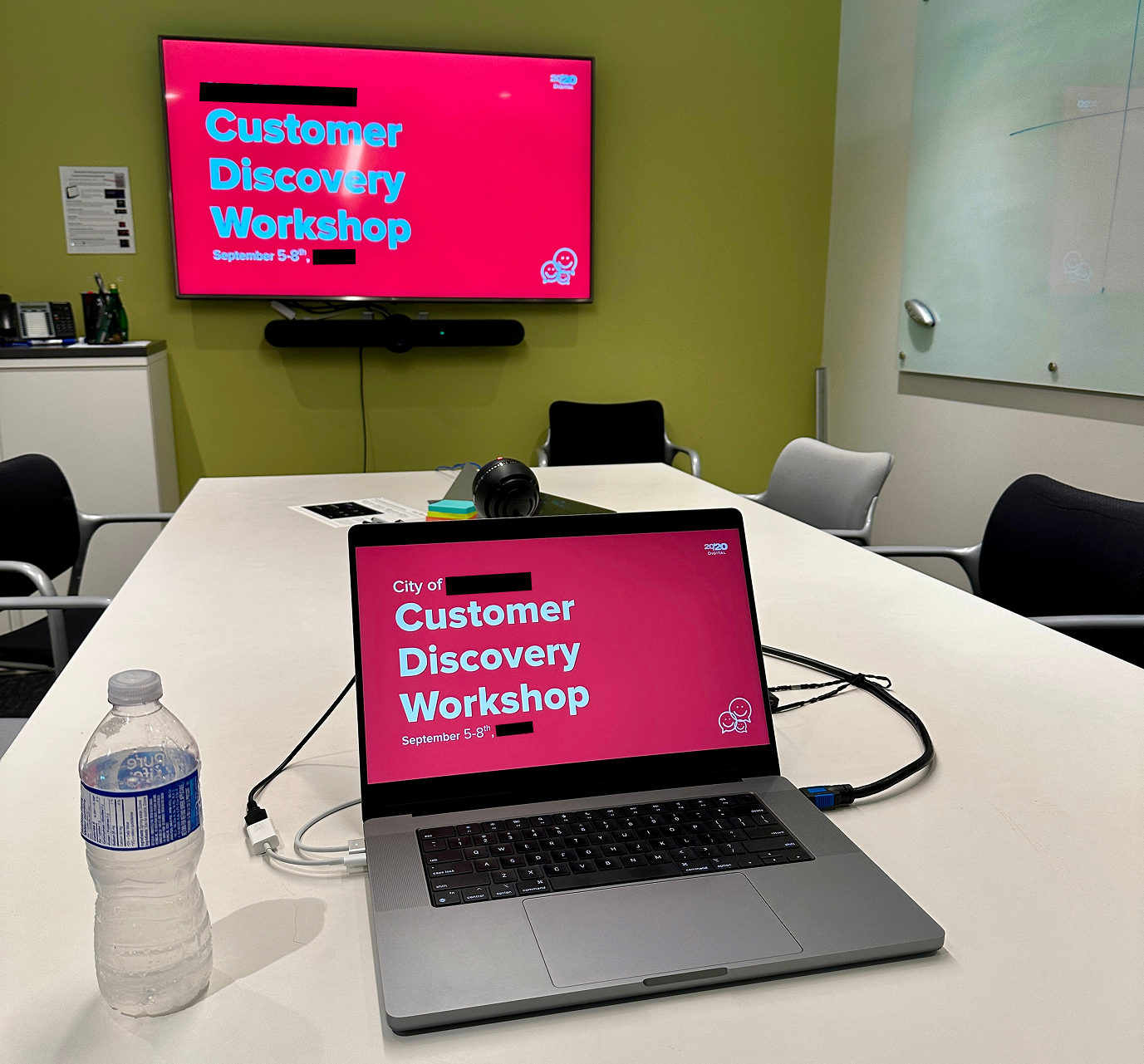 An open laptop on a boardroom table, displaying the title slide of a customer discovery workshop for a municipal government, with the city's name redacted.